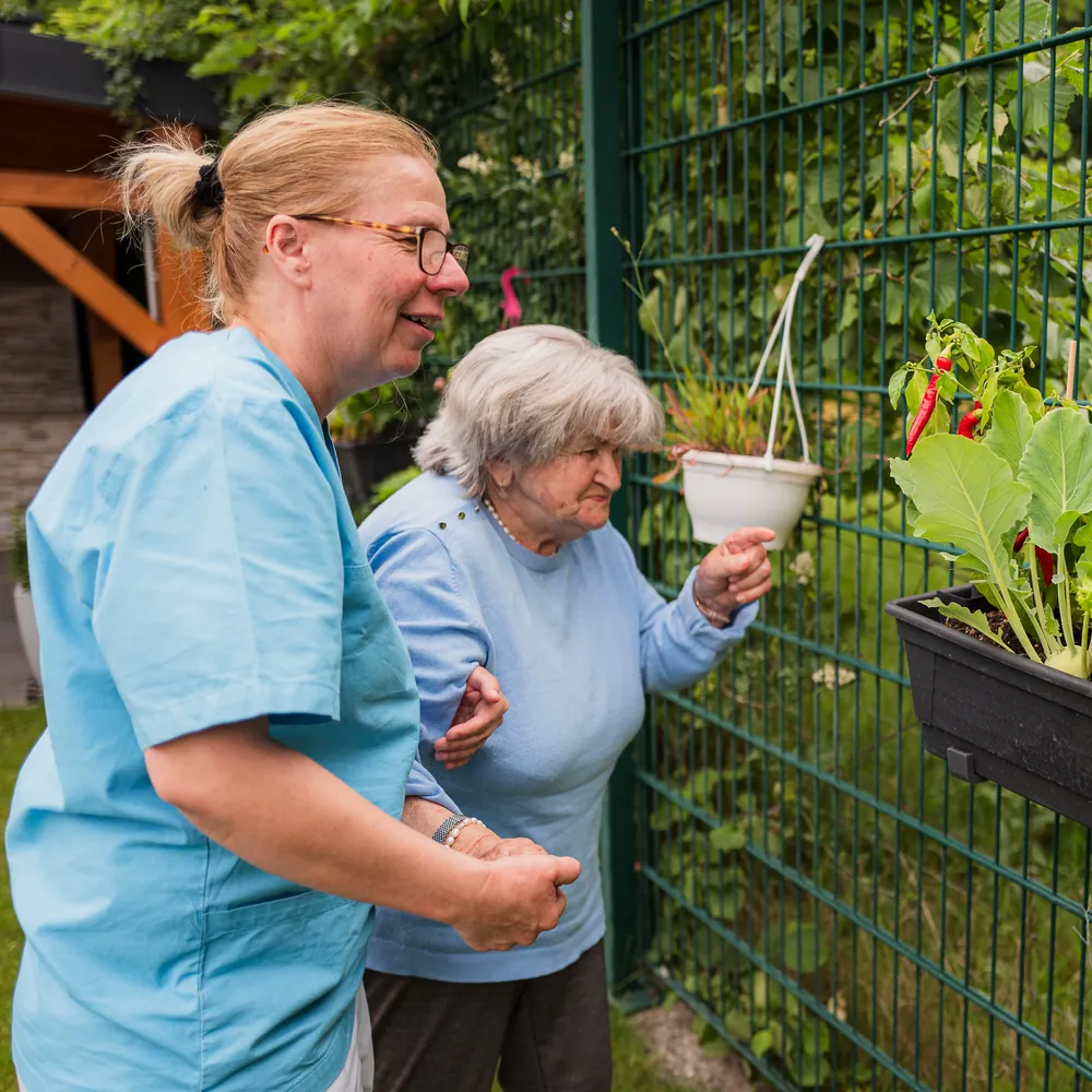 Eine Pflegerin und eine Seniorin schauen sich gemeinsam die Gemüsekästen im Garten an