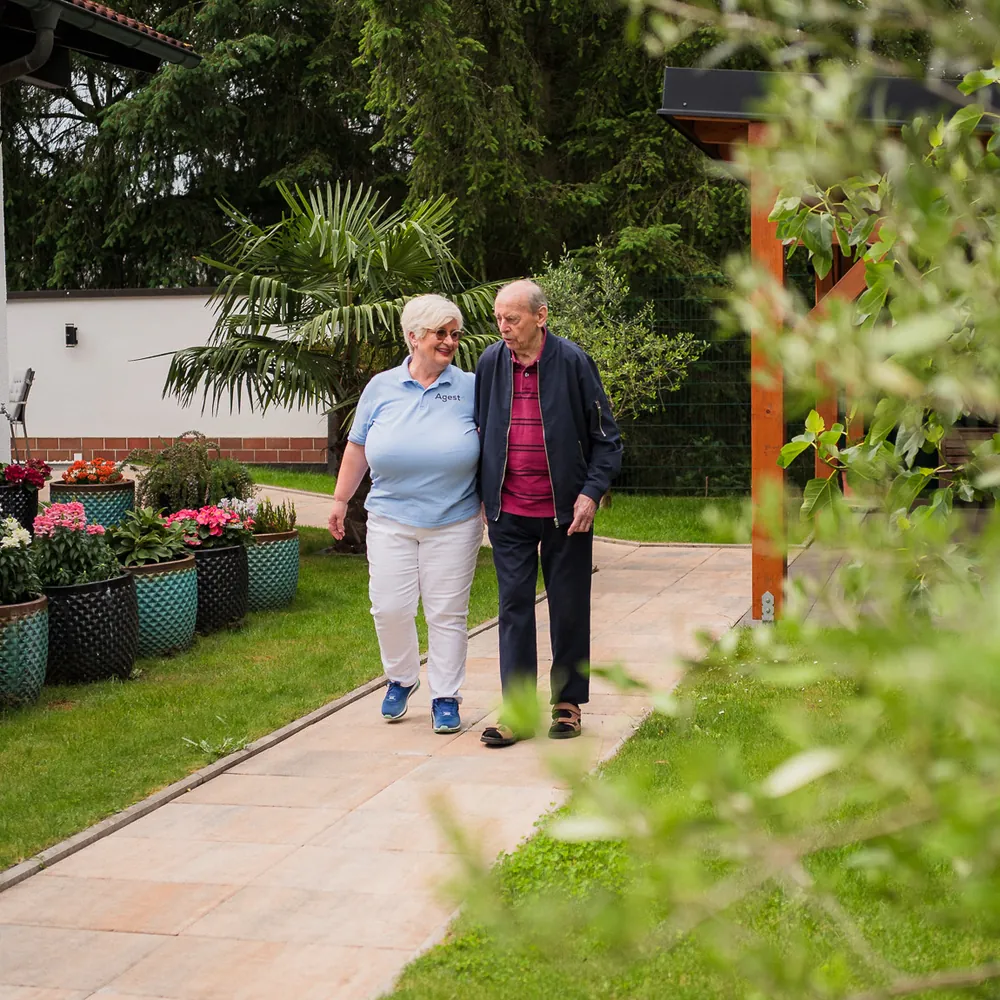 Eine Mitarbeiterin von Agesto geht mit einem Senior im Garten spazieren