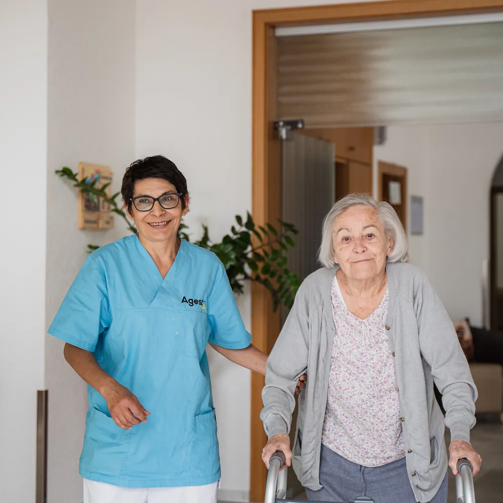 Eine Pflegerin von Agesto begleitet eine Seniorin mit Rollator